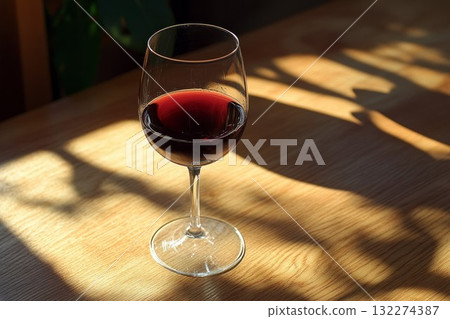 Elegant glass of red wine rests on rustic wooden table. Warm ambient lighting enriches deep red hue, creating cozy, inviting atmosphere. Neural network AI generated 132274387