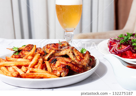 Delicious barbecue chicken wings, with French fries, salad and a refreshing drink, at a cozy table, there are no people 132275187