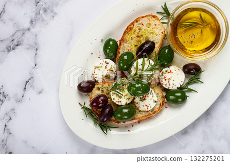 a plate with a snack, ciabatta bread with cheese and olives, olive oil, spices and herbs, top view, no people, 132275201