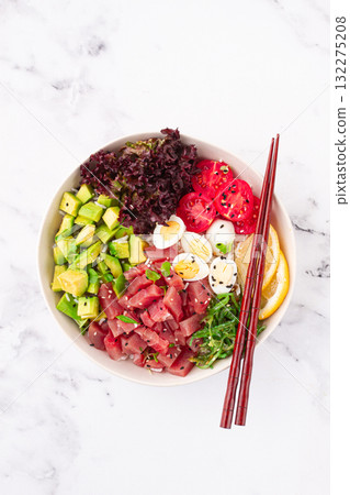 Fresh poke bowl, with tuna, avocado, and vegetables, served on a white plate Fresh poke bowl, with tuna, avocado, and vegetables, served on a white plate 132275208