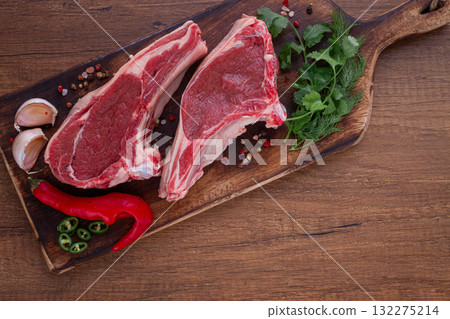 Freshly sliced lamb chops, with herbs and vegetables, on a wooden board, ready to cook, on a wooden table, 132275214