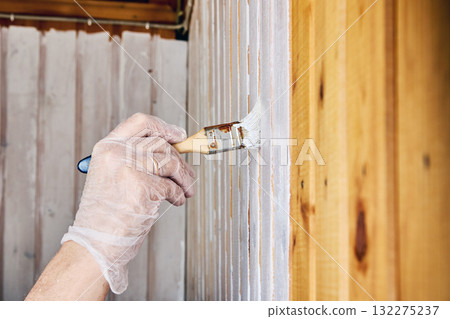 Painter uses paintbrush to apply white paint on wooden wall panels. 132275237
