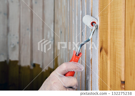 Applying white paint to vertical wooden wall slats with roller. Applying white paint to vertical wooden wall slats with roller. 132275238