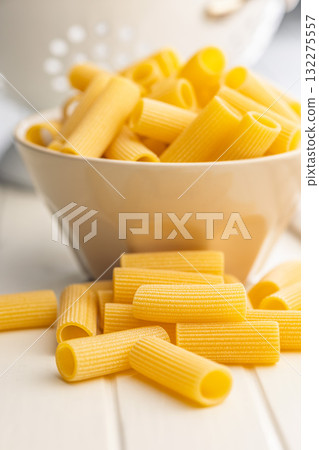 Uncooked rigatoni pasta on white table. Uncooked rigatoni pasta on white table. 132275557