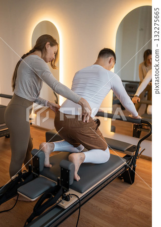 Woman Pilates Instructor Gives Guidance to a men Student While They Utilize the Reformers Equipment 132275665