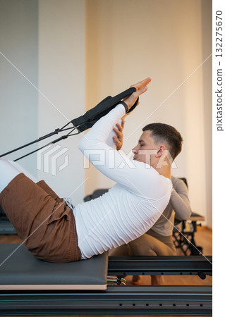 Woman Pilates Instructor Gives Guidance to a men Student While They Utilize the Reformers Equipment Woman Pilates Instructor Gives Guidance to a men Student While They Utilize the Reformers Equipment 132275670