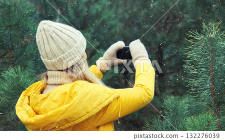 Young woman taking picture on phone Christmas tree in winter park, girl with smartphone in forest Young woman taking picture on phone Christmas tree in winter park, girl with smartphone in forest 132276039