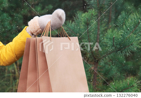Purchase, holidays, female hand holding showing paper shopping bags, gift against Christmas tree 132276040