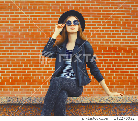 Stylish young woman model wearing black round hat, leather jacket in rock style on city street Stylish young woman model wearing black round hat, leather jacket in rock style on city street 132276052