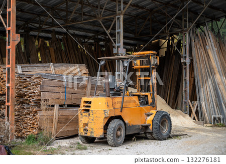 Old yellow forklift inside carpentry workshop with wooden planks and construction materials Old yellow forklift inside carpentry workshop with wooden planks and construction materials 132276181