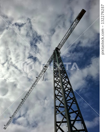 A tall construction crane towers against a backdrop of clouds, showcasing the scale and structure of the ongoing building project from an upward angle. 132276287