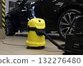 A yellow vacuum cleaner near a car on the garage floor before cleaning  132276480