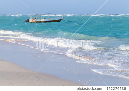 A small motor boat floats off a white sandy beach as turquoise waves A small motor boat floats off a white sandy beach as turquoise waves 132276586