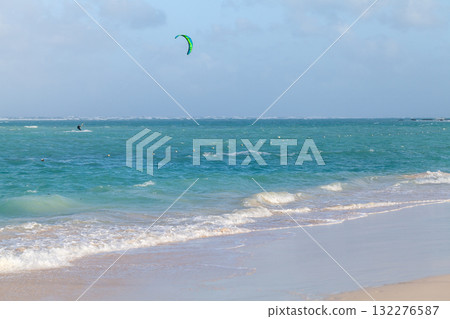 Beach scene with a lone kite surfer glides across turquoise waves 132276587