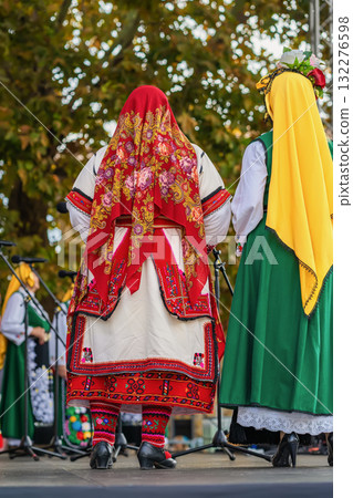 Women dressed in colorful traditional folk costumes perform on an outdoor stage during a cultural festival. Concept of tradition and culture, folk costume, cultural heritage, national identity 132276598
