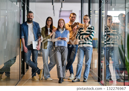 Group of young business team walking together through a modern office hallway, smiling and discussing work. Concept of confidence, teamwork, leadership, and positive workplace culture. 132276967