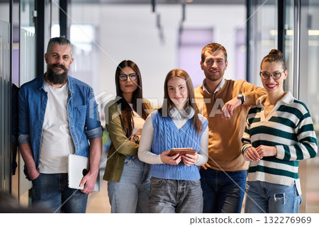 Group of young business team walking together through a modern office hallway, smiling and discussing work. Concept of confidence, teamwork, leadership, and positive workplace culture. 132276969