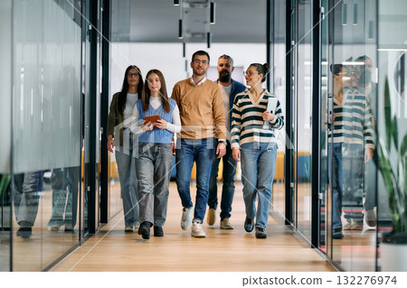 Group of young business team walking together through a modern office hallway, smiling and discussing work. Concept of confidence, teamwork, leadership, and positive workplace culture. Group of young business team walking together through a modern office hallway, smiling and discussing work. Concept of confidence, teamwork, leadership, and positive workplace culture. 132276974