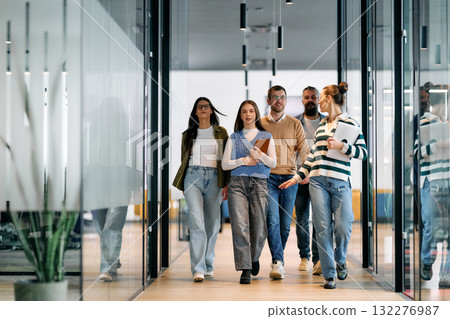 Group of young business team walking together through a modern office hallway, smiling and discussing work. Concept of confidence, teamwork, leadership, and positive workplace culture. Group of young business team walking together through a modern office hallway, smiling and discussing work. Concept of confidence, teamwork, leadership, and positive workplace culture. 132276987