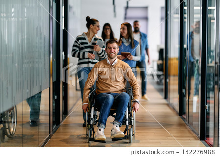 Group of diverse business people walking together in a modern office hallway, led by a confident smiling man in a wheelchair, representing inclusion, equality, and teamwork. 132276988