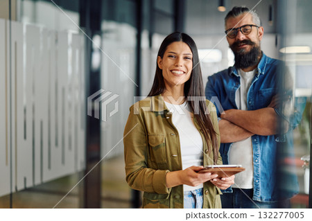 Two business professionals having a focused discussion while reviewing information on a tablet in a bright modern office hallway, symbolizing teamwork, communication, and digital collaboration. Two business professionals having a focused discussion while reviewing information on a tablet in a bright modern office hallway, symbolizing teamwork, communication, and digital collaboration. 132277005