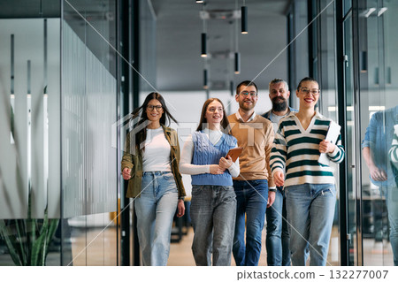 Group of young business team walking together through a modern office hallway, smiling and discussing work. Concept of confidence, teamwork, leadership, and positive workplace culture. 132277007