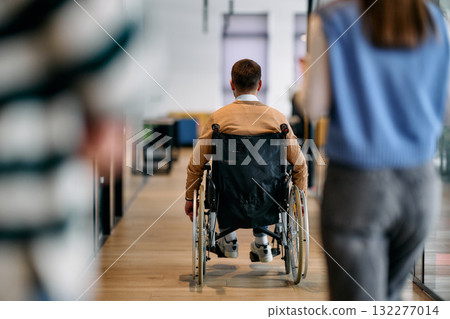 Confident businessman in a wheelchair moving independently through a modern office corridor, symbolizing accessibility, inclusion, and determination in the workplace. 132277014