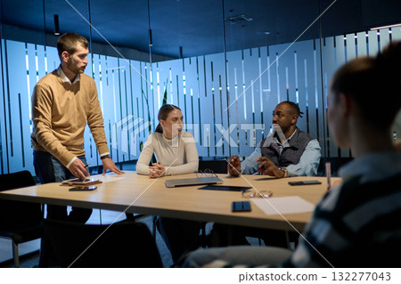 Group of diverse coworkers having a serious discussion around a conference table, led by a bearded male manager, representing teamwork, leadership, and strategy development in a modern business 132277043