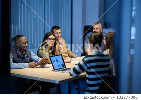 Diverse business team gathered around a table discussing analytics during a meeting in a modern office. Laptop screen shows charts and graphs, symbolizing teamwork, communication, and data driven 132277096