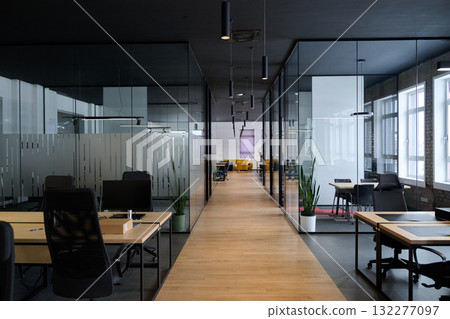 Contemporary open space office interior with minimalist design, black chairs, wooden desks, and glass partitions, representing a professional corporate workspace environment. 132277097