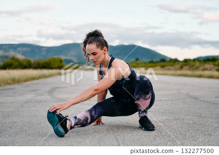Determined Female Athlete Stretching After an Intense Run Through Rugged Mountain Terrain. 132277500