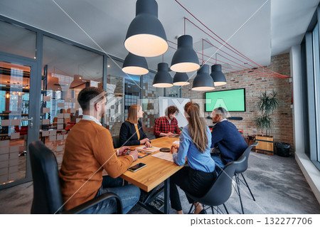 In the vibrant ambiance of a modern startup office, a diverse team of business professionals engage in discussions on various projects and develop new business strategies, epitomizing creativity and 132277706