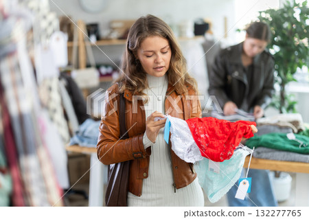 Happy young female customer dressing in ordinary clothes choosing underwear and holding panties in hands in store 132277765