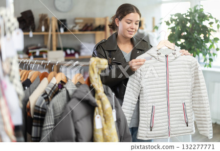 Positive young girl choosing down jacket in clothing store Positive young girl choosing down jacket in clothing store 132277771