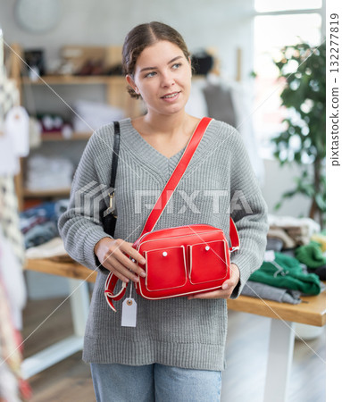 Positive young girl choosing handbag in clothing store 132277819