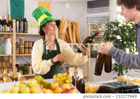 Female vendor in Irish green cap offers Irish ale to male customer 132277949