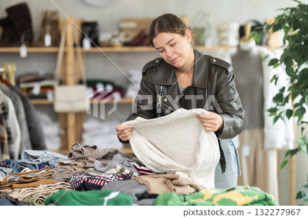 Young woman chooses sweater in clothing store Young woman chooses sweater in clothing store 132277967