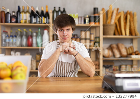 Portrait of confident young salesperson sitting at counter in supermarket 132277994