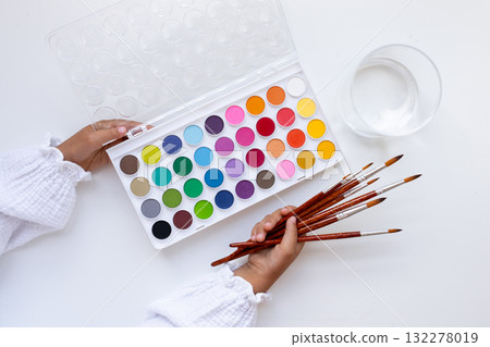 Child hand holding paintbrushes and vibrant watercolor palette on white background Child hand holding paintbrushes and vibrant watercolor palette on white background 132278019