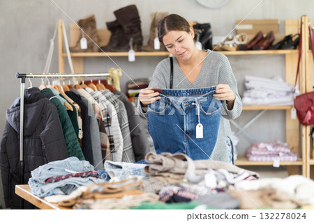 Uncertain young girl choosing jean pantaloons in clothing store 132278024