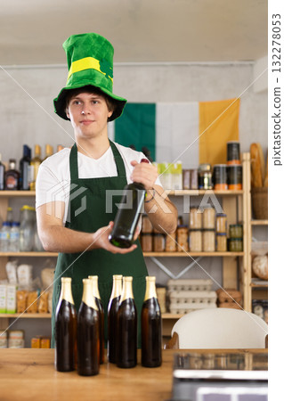 Positive male store clerk in green hat is preparing to meet customers on eve of St. Patricks Day. 132278053