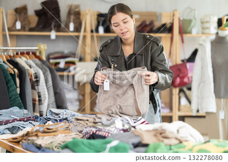 Focused young girl client selecting trousers in clothing shop. Sale of winter clothing collection 132278080