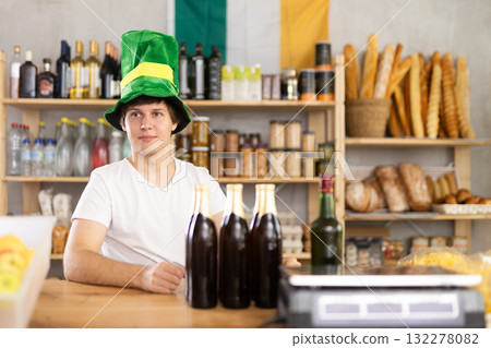Positive male store clerk in green hat is preparing to meet customers on eve of St. Patricks Day. 132278082