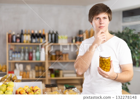 Grocery shopping - guy chooses canned olives in supermarket Grocery shopping - guy chooses canned olives in supermarket 132278148