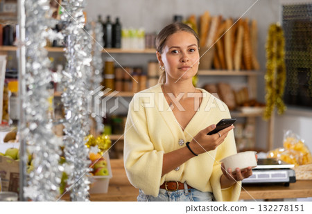Young woman in store chooses cottage cheese, scan product label with phone 132278151