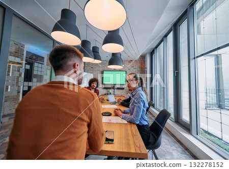 In the vibrant ambiance of a modern startup office, a diverse team of business professionals engage in discussions on various projects and develop new business strategies, epitomizing creativity and 132278152