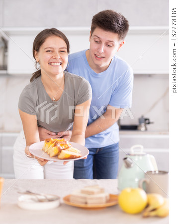 Cheerful young couple preparing table for tea-time in home kitchen Cheerful young couple preparing table for tea-time in home kitchen 132278185