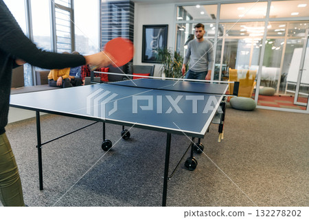 Business colleagues take a break from work to enjoy a game of table tennis, fostering teamwork and camaraderie in the workplace 132278202