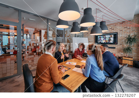 In the vibrant ambiance of a modern startup office, a diverse team of business professionals engage in discussions on various projects and develop new business strategies, epitomizing creativity and 132278207