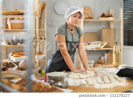 Young baker girl is standing near work table in kitchen, working with dough 132278227